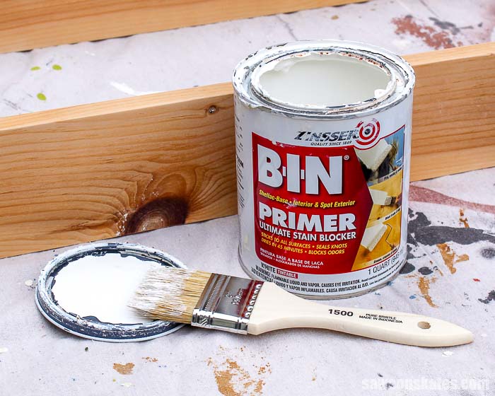 A container of BIN primer, paintbrush and a wood knot.