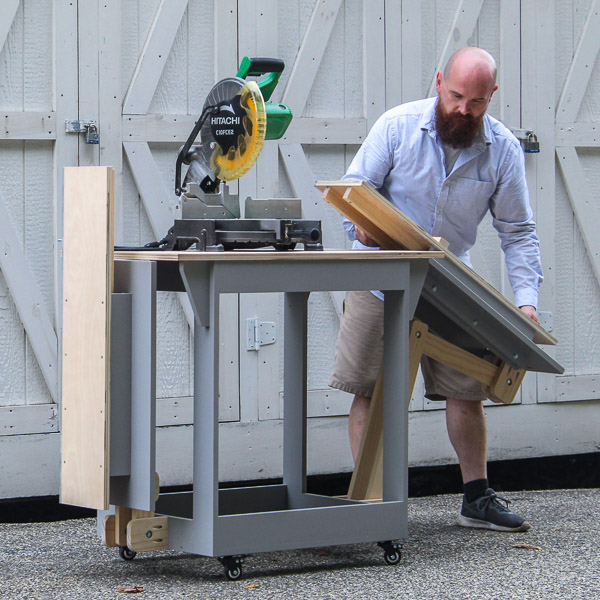 Person raising the arm of a folding miter saw stand