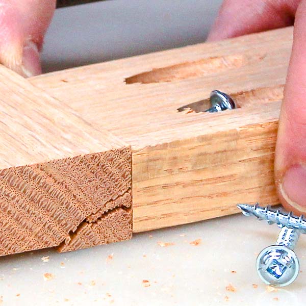 A pocket screw splitting a pocket hole in a piece of oak