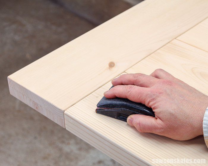 Using a sanding block on a DIY farmhouse table top with breadboard ends