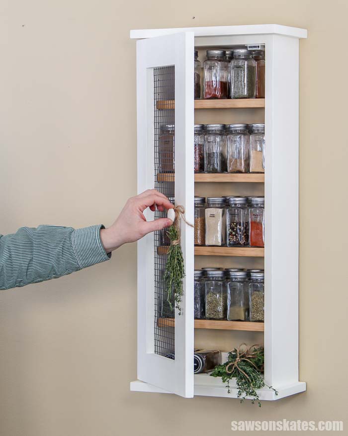 Build your own wall-mounted DIY spice rack with these free plans! This easy to build wood cabinet has a rustic chicken wire door and adjustable shelves.