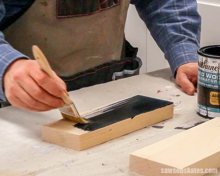 Using a paintbrush to apply a charred wood accelerator to a piece of pine