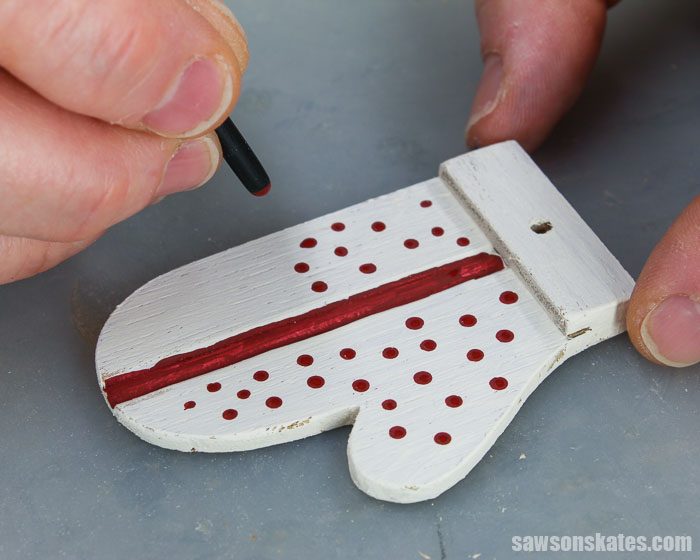 Using a paintbrush to make polka dots on a homemade mitten Christmas tree ornament