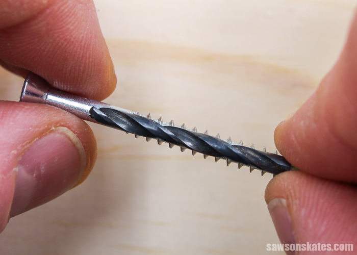 Holding a drill bit over a screw to determine the size of drill bit needed to drill a countersink hole