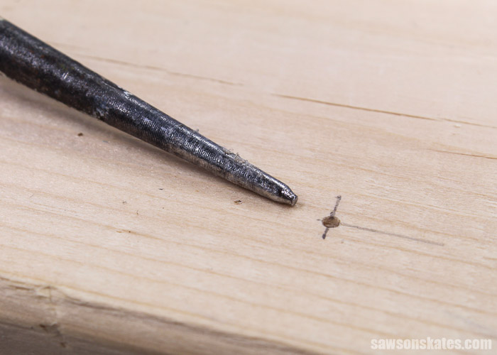 The point of an awl next to a hole in wood made by the awl