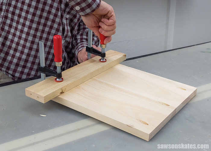 Clamping a piece of scrap wood to the side panel of a DIY sandpaper organizer