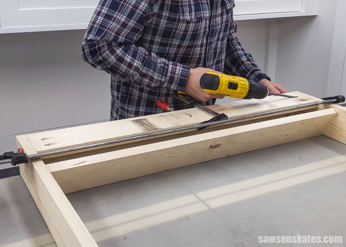 Using a drill to attach the back rail on a DIY paint storage rack
