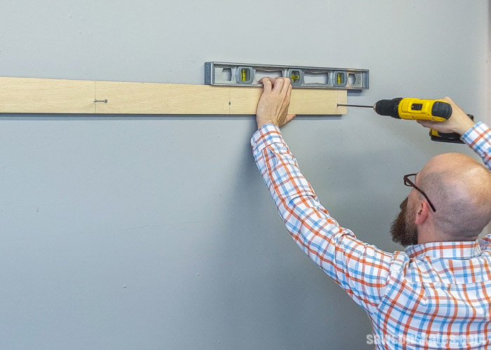 Using a drill to drive a screw to attach a board to the wall