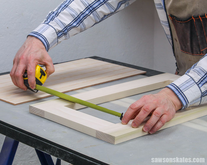 Using a tape measure to determine the size of an opening in a cabinet door