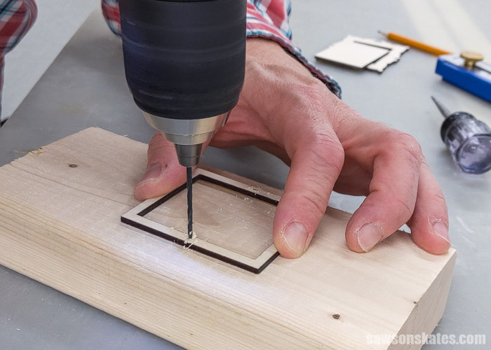 Using a drill to make holes for turn buttons that will attach the back to a DIY Christmas picture frame ornament