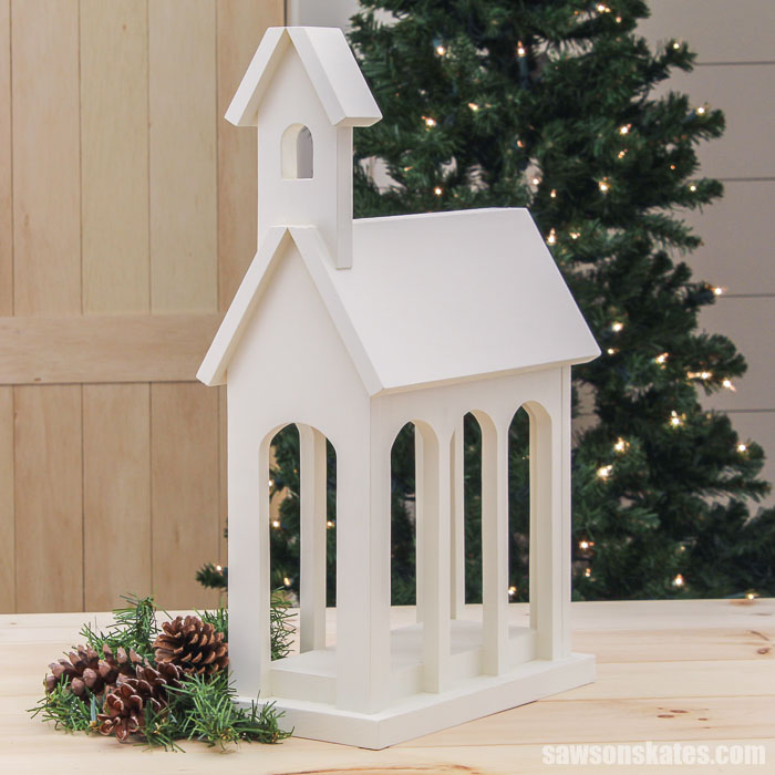 Side view of a DIY Christmas card display shaped like a church in front of a Christmas tree