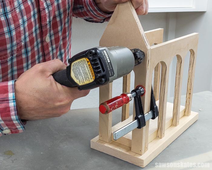 Using a brad nailer to attach the front to a DIY Christmas card display shaped like a church