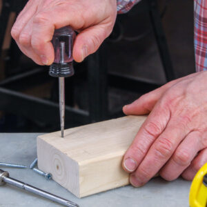 Hand pushing an awl into a piece of wood