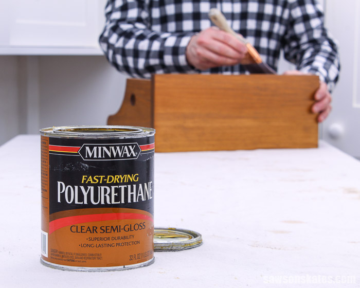 Can of polyurethane in the foreground and hand with a paintbrush in the background