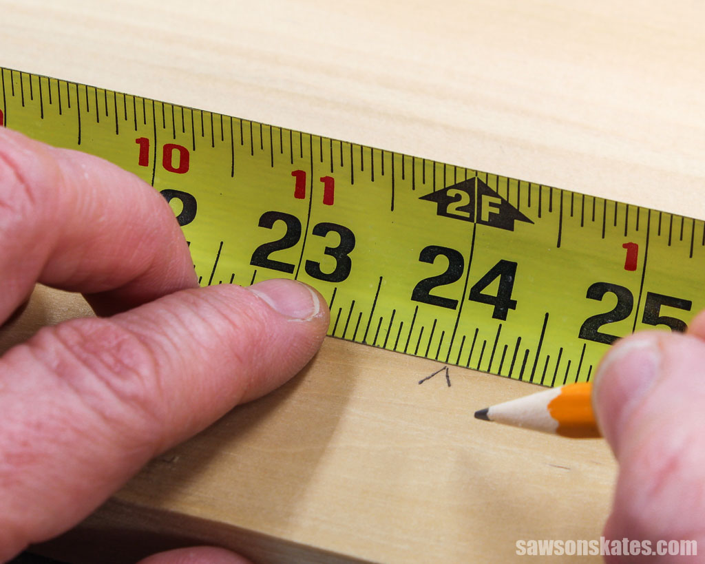 Using a pencil to mark a "V" on a board next to a tape measure