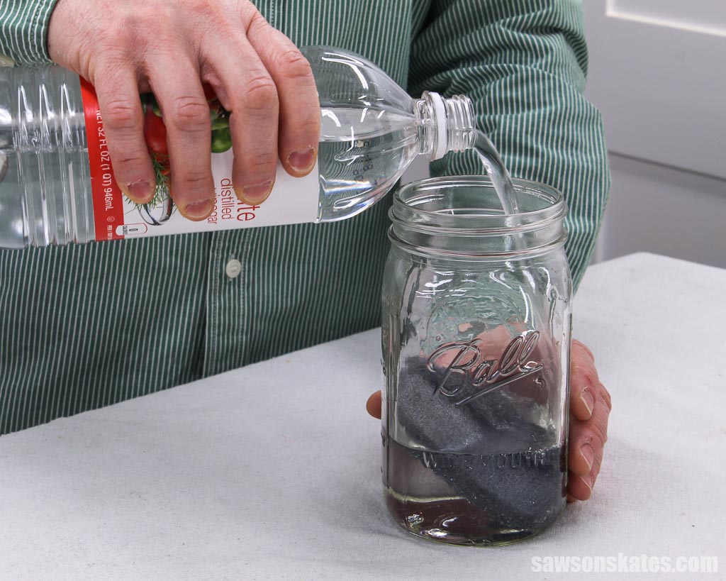 Pouring vinegar into a jar with a steel wool pad to make a natural wood stain