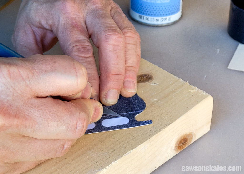 Using an X-Acto knife to cut the small inner areas between the posts on a template for a DIY ice skate ornament