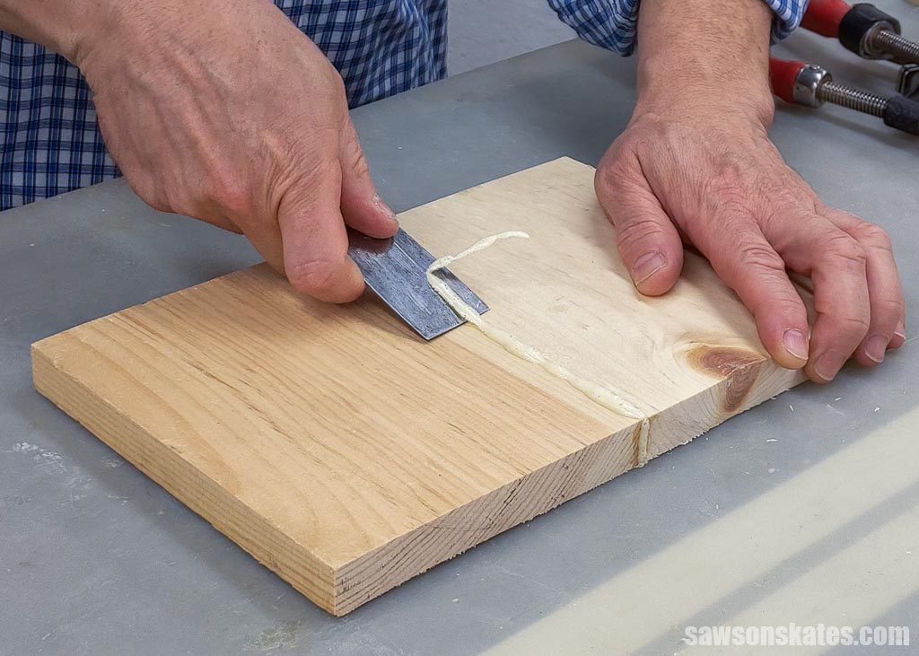 Using a putty knife to remove the excess polyurethane glue that expanded out of the joint
