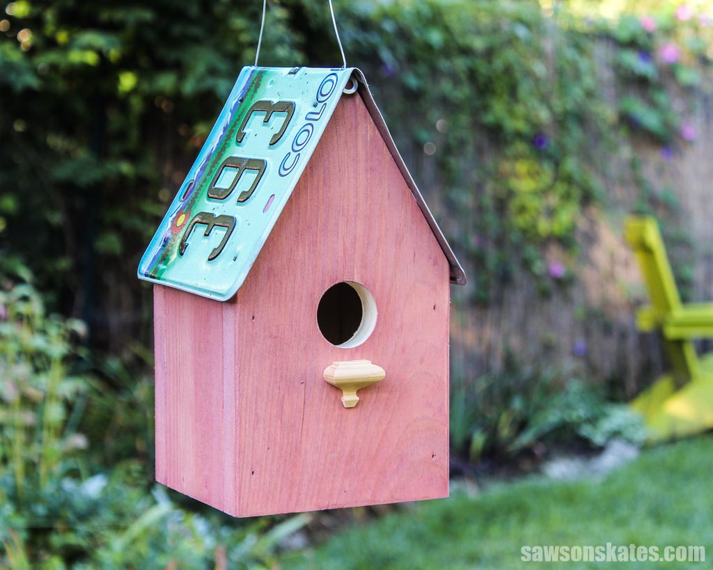 DIY license plate birdhouse with fence in the background