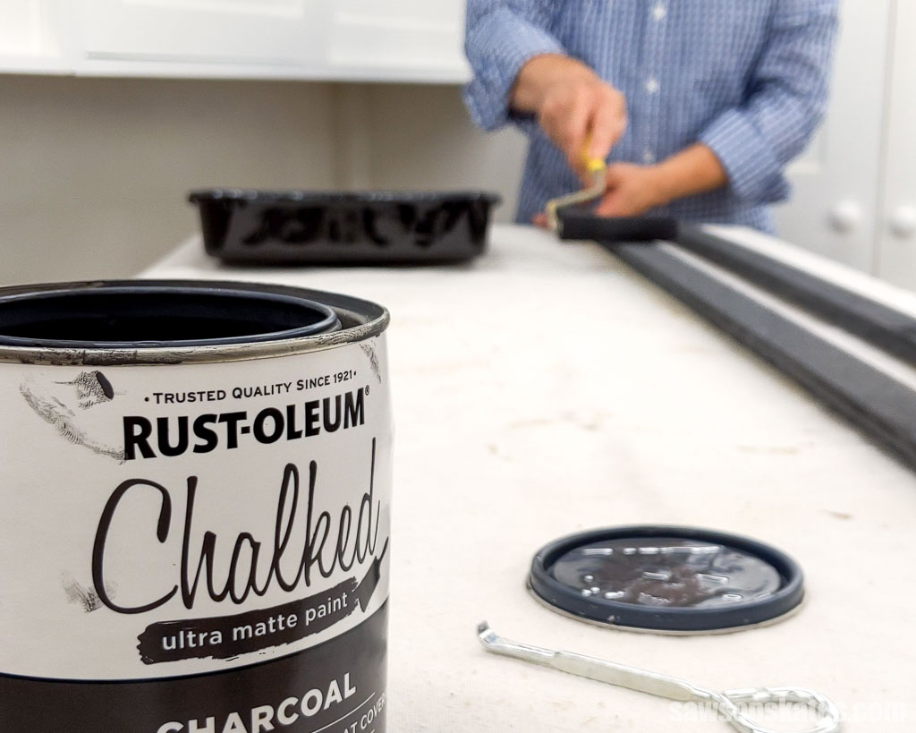A can of chalk-type pain the foreground and paint roller is being used in the background to apply the paint to strips of wood