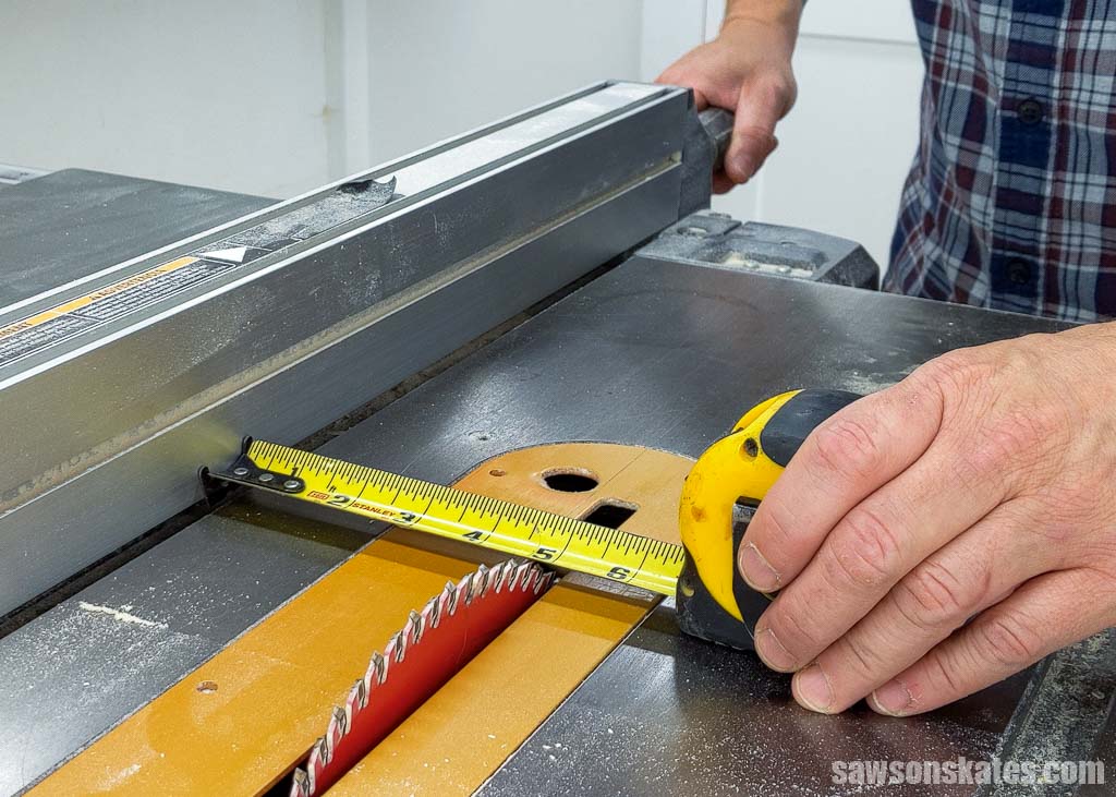 Hand using a tape measure to set the rip fence on a table saw