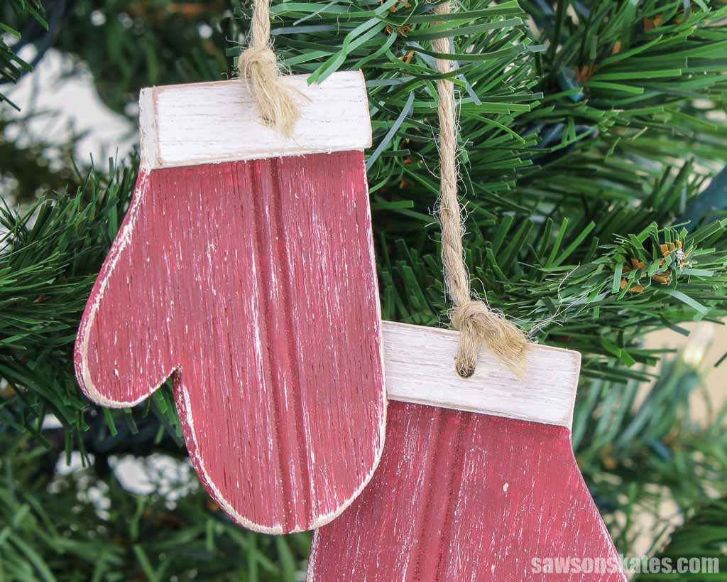 Red wood mitten ornament with a white cuff hanging in a Christmas tree