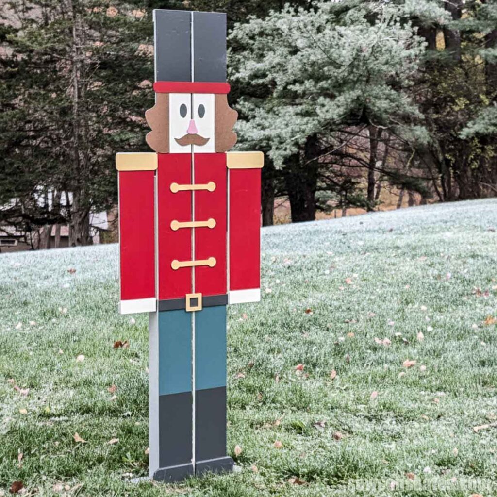 Six-foot-tall DIY nutcracker standing in a yard lightly covered with snow