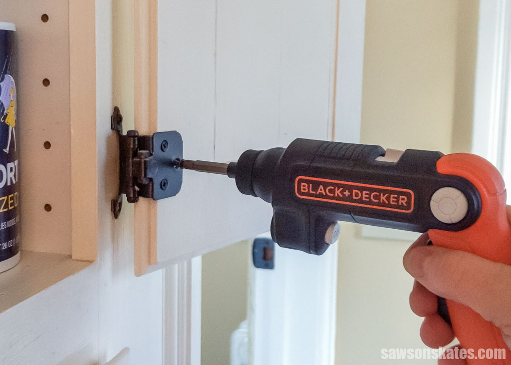 Using an electric screwdriver to tighten a cabinet hinge