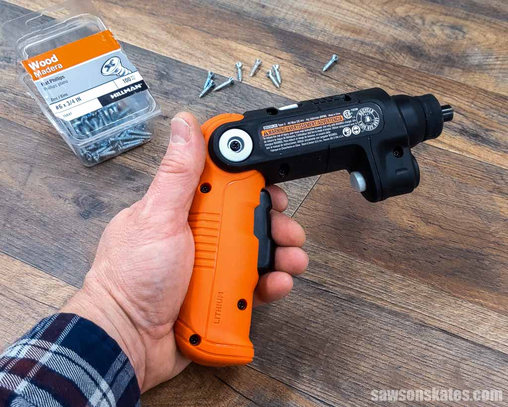 Hand holding an electric screwdriver with a package of screws in the background