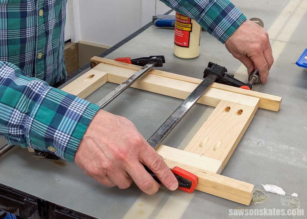 Hands adjusting woodworking clamps a around a picture frame