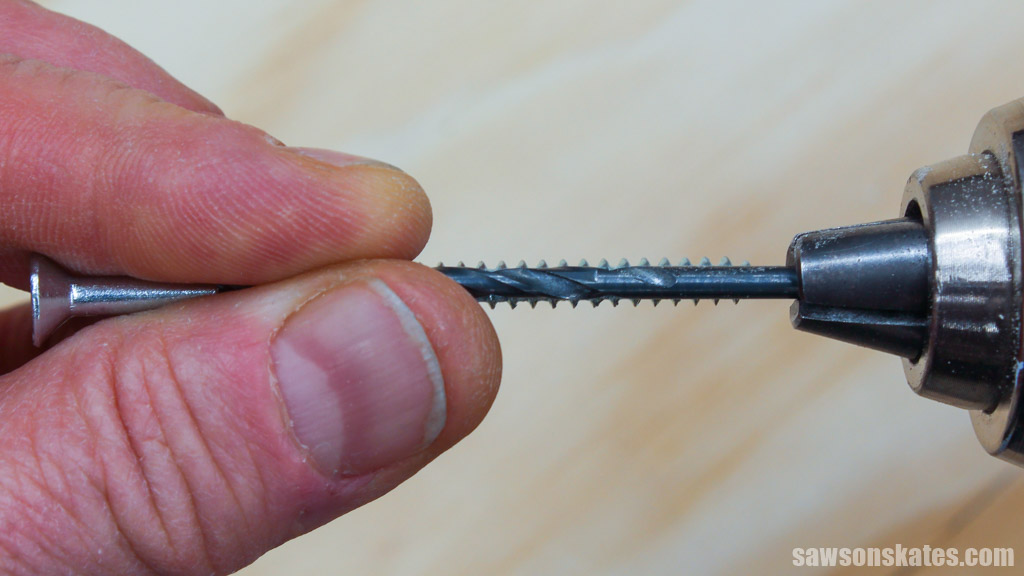 Fingers holding a screw under a drill bit to determine what size bit is needed to make a pilot hole