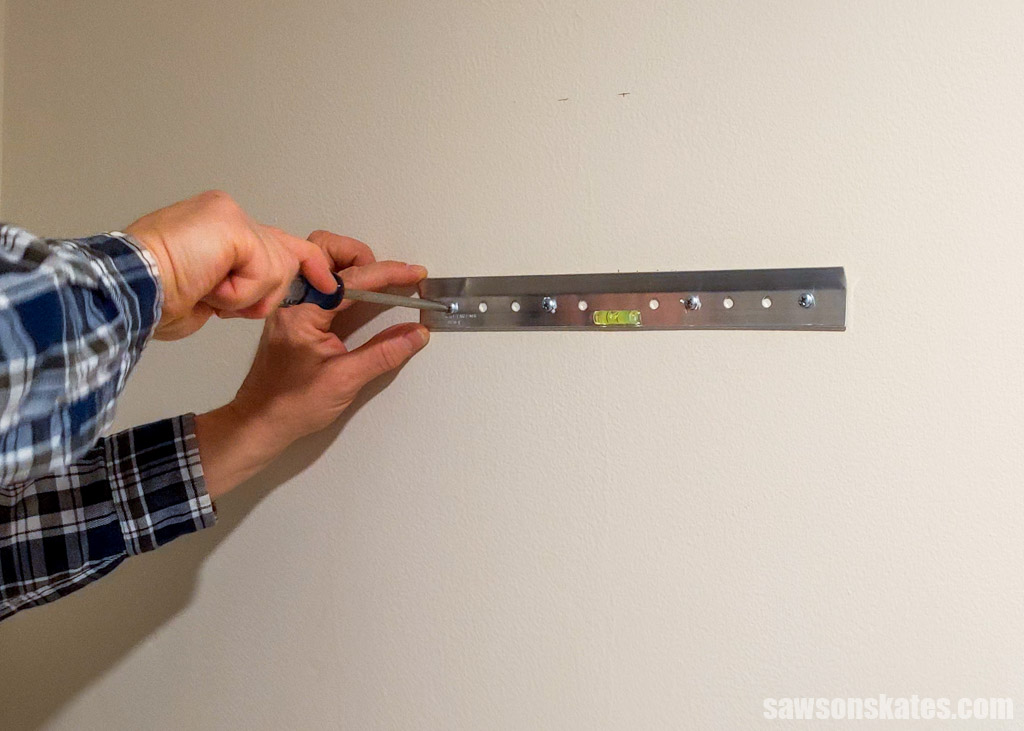 Hands using a screwdriver to attach a hanger on a wall