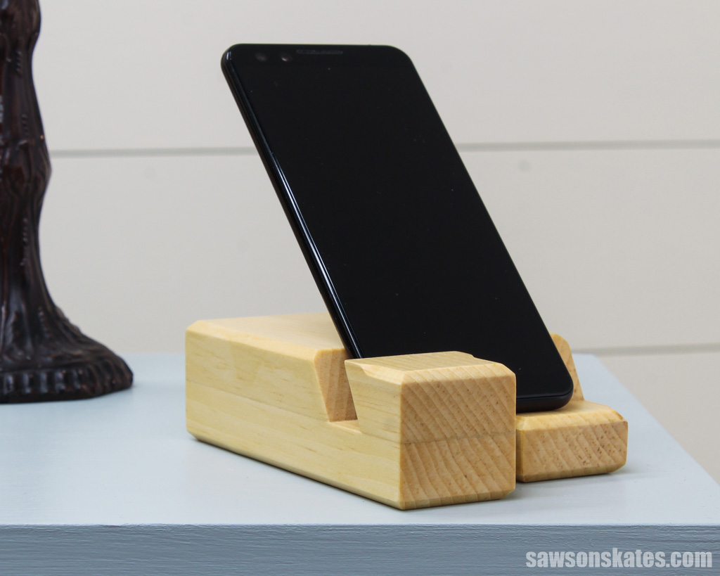 DIY wooden phone holder on a nightstand with a lamp on the left