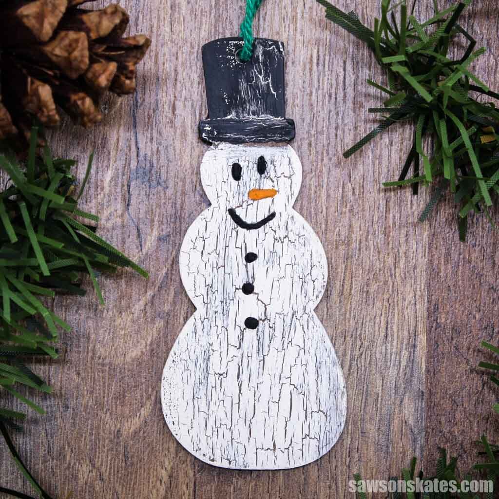 DIY wooden snowman Christmas ornament on a piece of wood surrounded by green tree branches