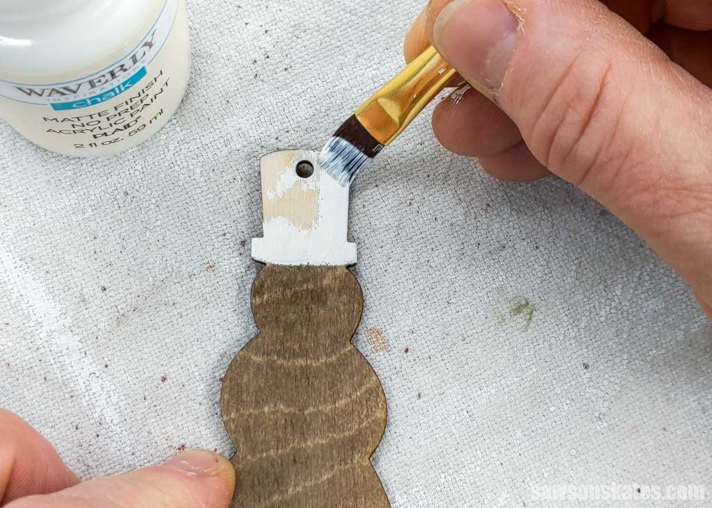 Using a brush to paint the hat of a wooden DIY snowman ornament