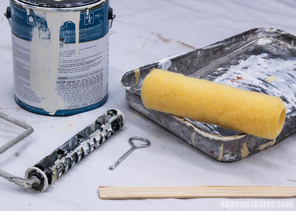Paint roller cover, roller frame, tray and paint can on a drop cloth