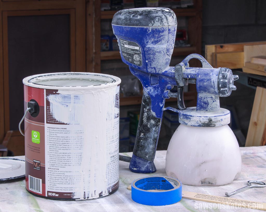Blue paint sprayer on a workbench next to an open can of paint