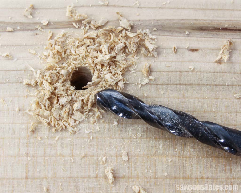 Black twist drill bit next to a hole in wood