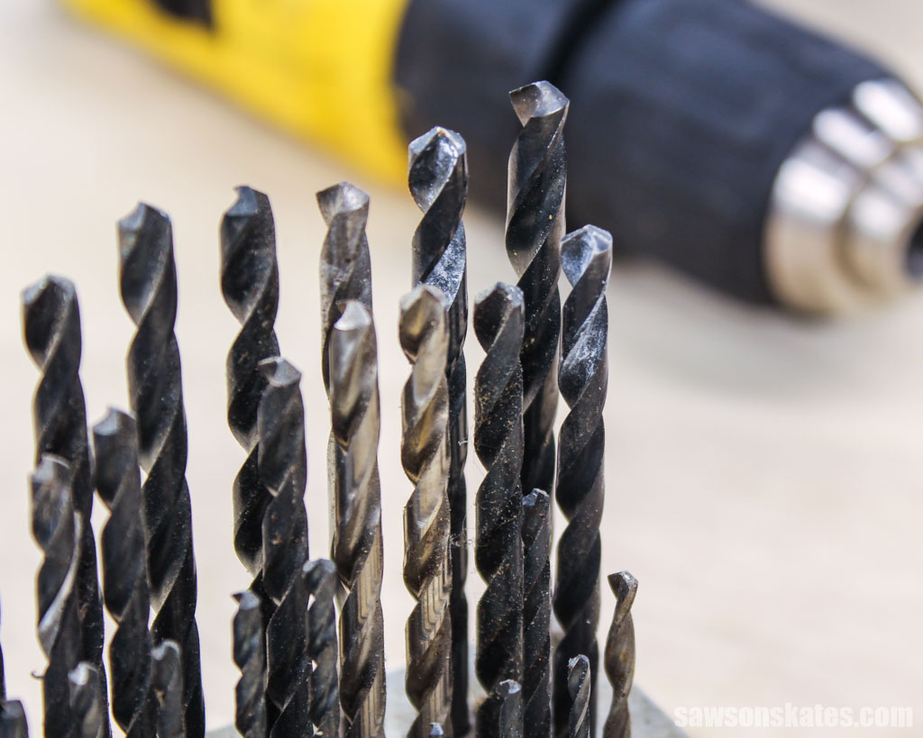 Several drill bits standing upright in the left corner with blurry drill in the background