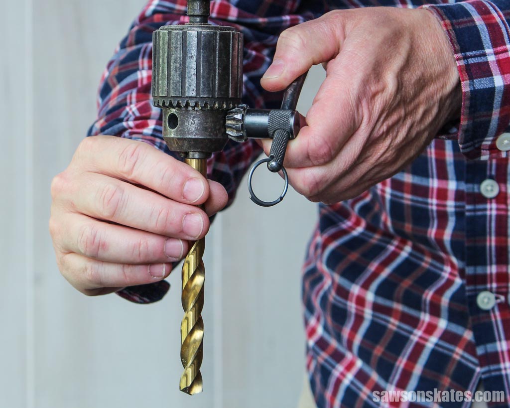 Holding a drill bit in one hand while tightening a drill's chuck around it using a chuck key