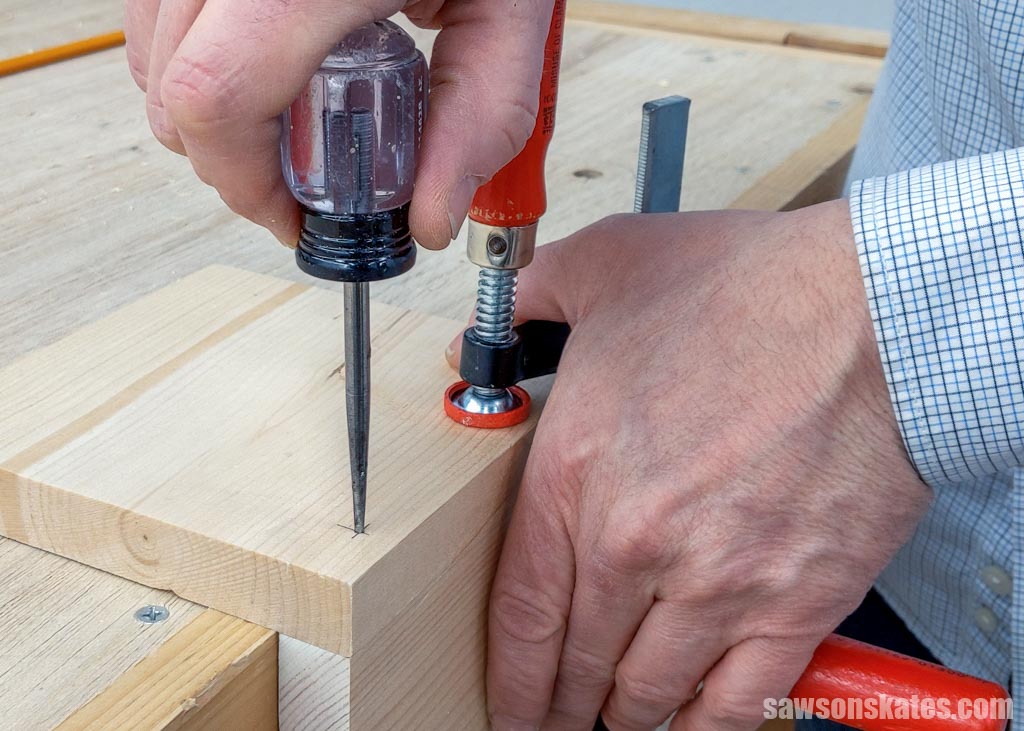 Hand pushing an awl into a piece of wood to make starting point for a drill bit