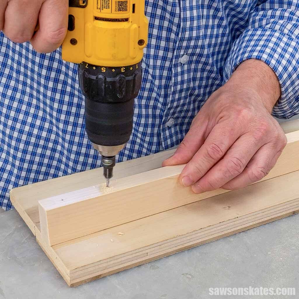 Hand holding a board while using a drill to make a hole