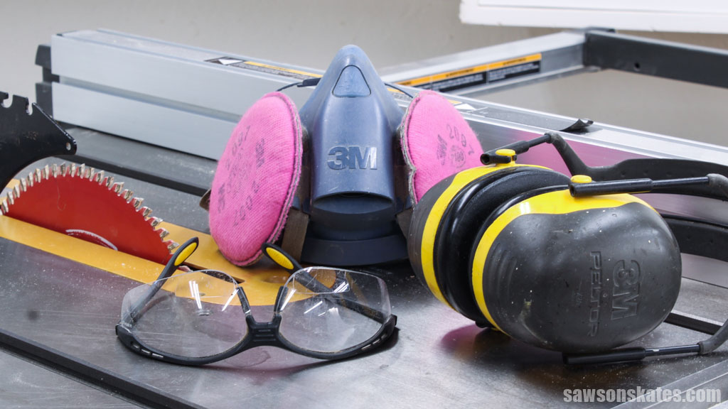 Safety glasses, respirator and earmuffs sitting on top of a table saw
