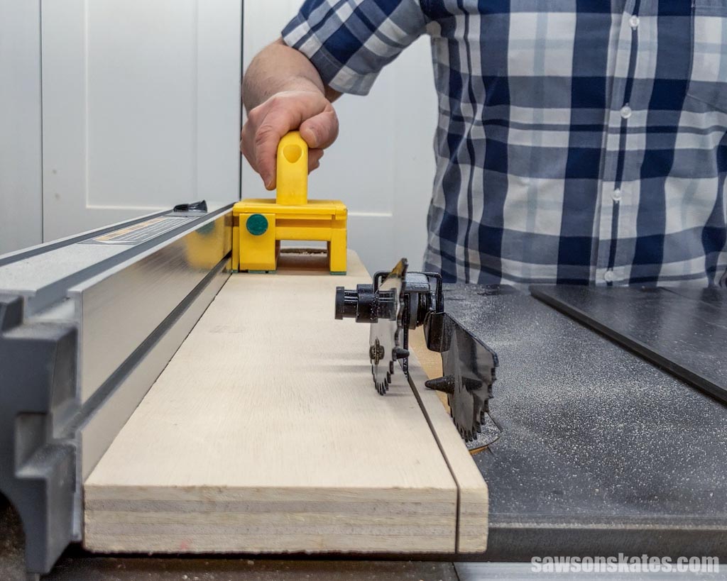 Person standing out of the path of a table saw's blade while feeding a piece of plywood with a push block