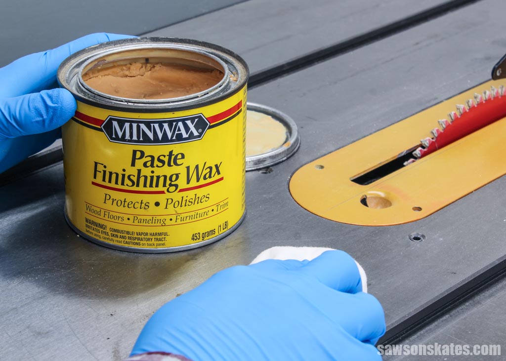 Hand applying wax to table saw's top with a can of paste wax in the background