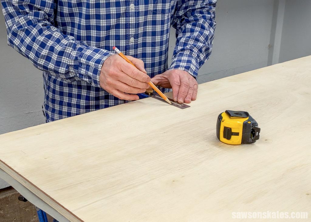 Using a pencil to mark the location for pocket holes on a piece of plywood for a DIY utility cart