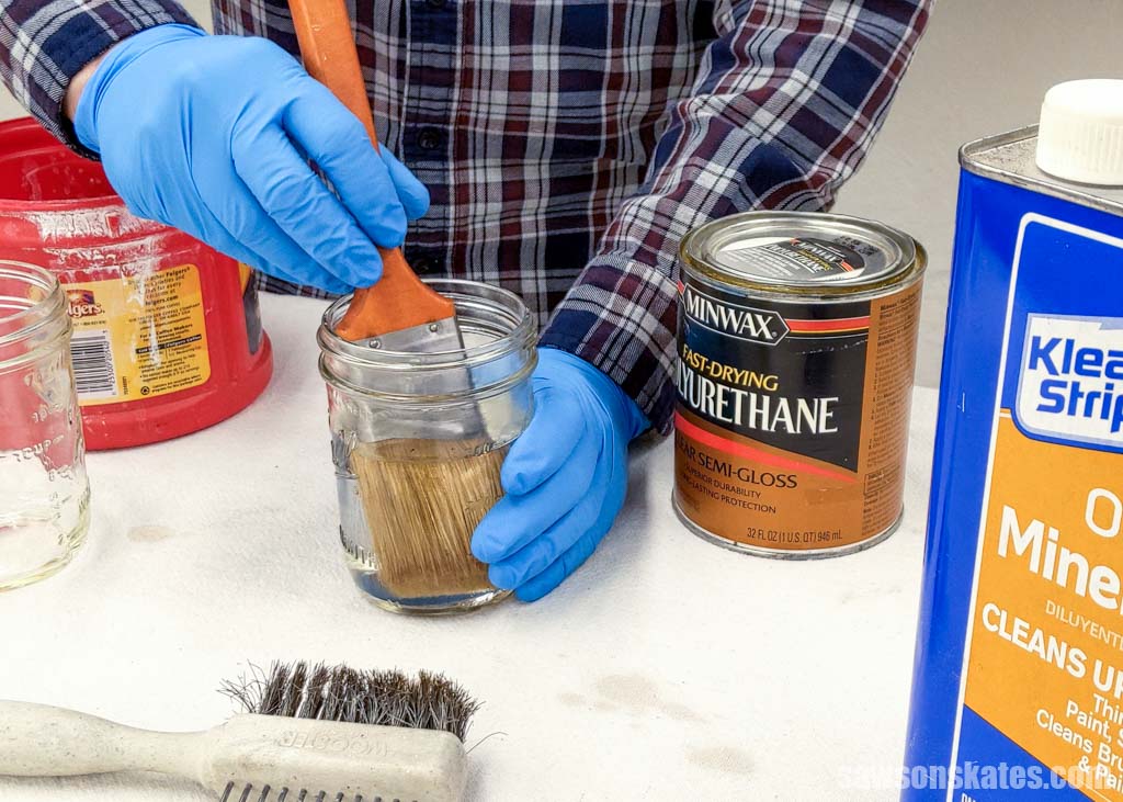 Hands wearing gloves cleaning a paint brush with mineral spirits in a mason jar