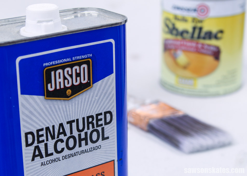 Container of denatured alcohol in the foreground with a paint brush and container of shellac in the background