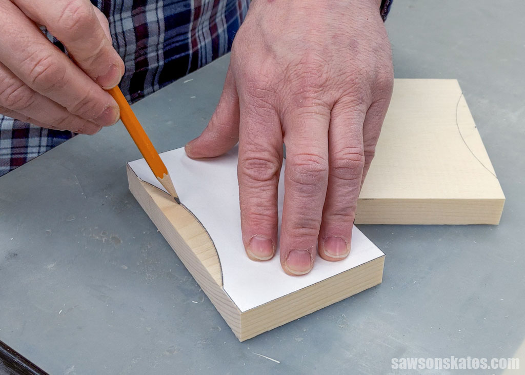 Hand using a pencil to trace a leg pattern onto a piece of wood