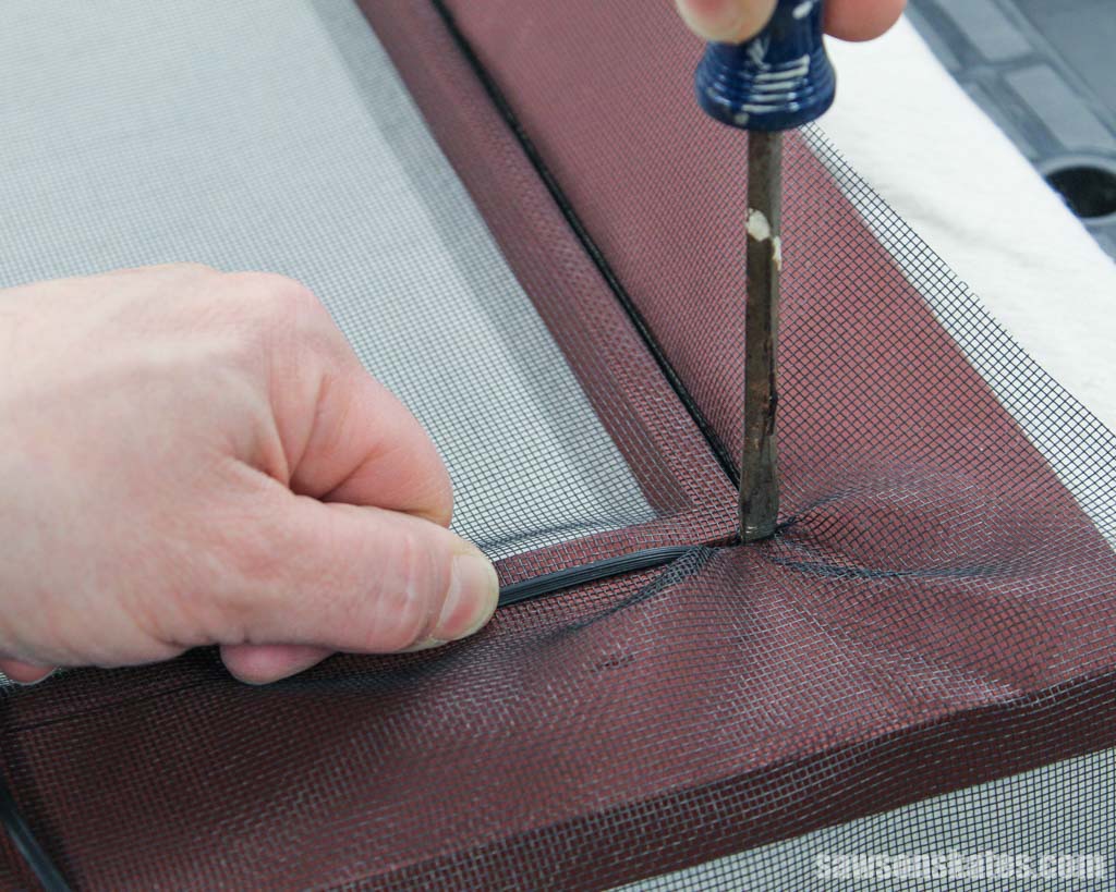 Using a screwdriver to insert spline into the corner of a window screen frame's channel
